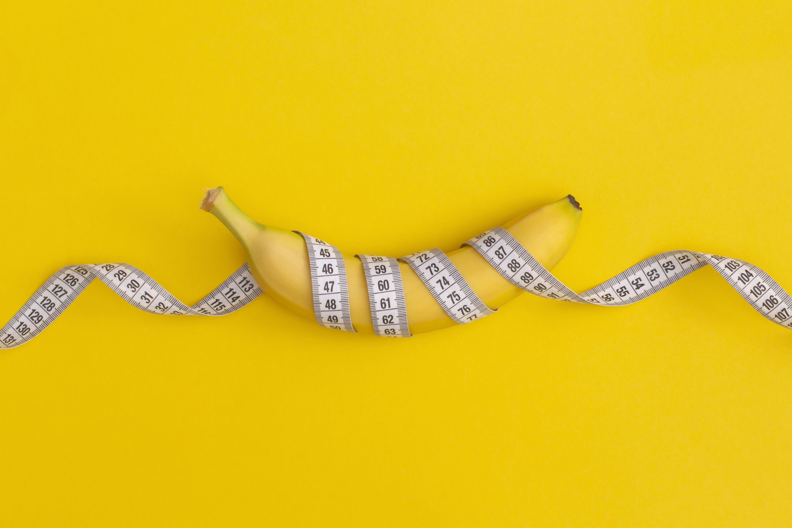Measuring tape and banana on yellow background. Weight loss concept | FitMeals4U